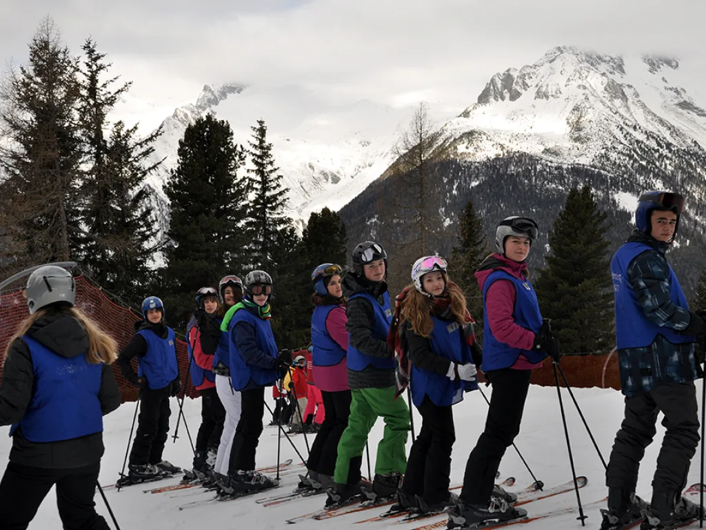 Skigruppe steht auf der Piste vor schneebedeckten Gipfeln.